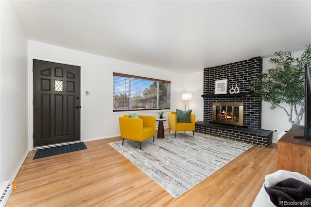 living room featuring wood-type flooring, a baseboard radiator, and a brick fireplace