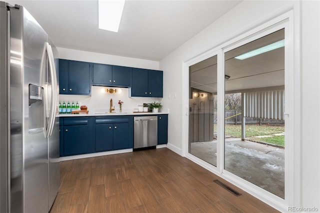 kitchen with sink, blue cabinets, dark wood-type flooring, and appliances with stainless steel finishes