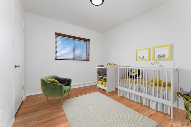 bedroom with wood-type flooring, a baseboard radiator, and a nursery area