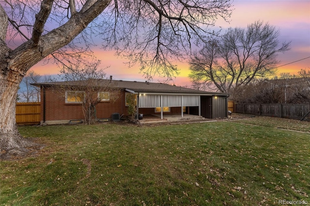 back house at dusk featuring a yard, a patio, and central AC