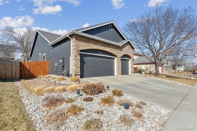 view of home's exterior with a garage, stone siding, driveway, and fence