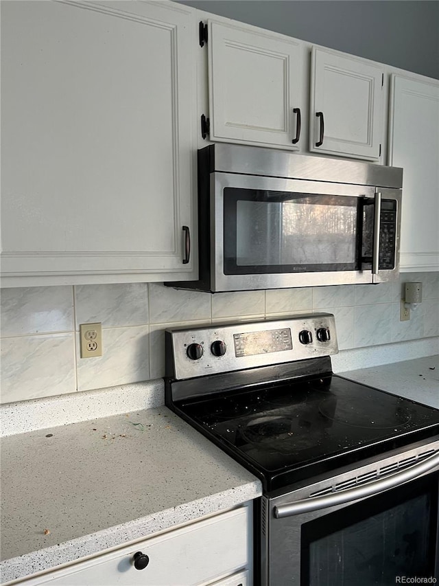 kitchen with tasteful backsplash, white cabinets, and appliances with stainless steel finishes