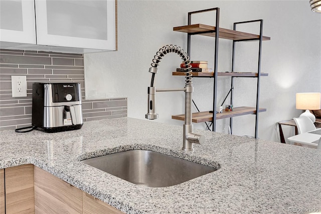 interior space with decorative backsplash, light stone counters, sink, and light brown cabinetry