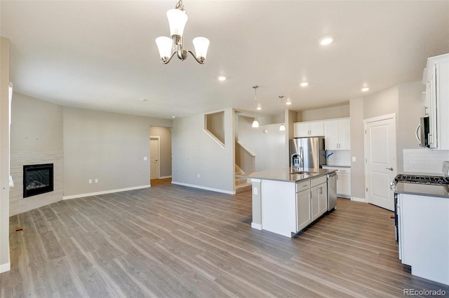 kitchen with stainless steel appliances, decorative light fixtures, white cabinets, light hardwood / wood-style floors, and an island with sink