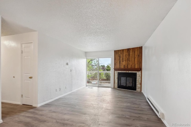 unfurnished living room featuring baseboard heating, a textured ceiling, wood finished floors, baseboards, and a tiled fireplace