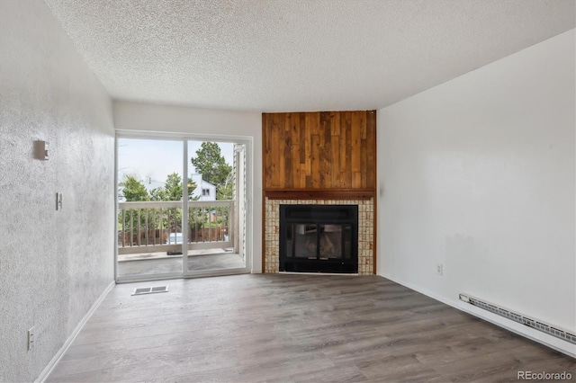 unfurnished living room featuring baseboard heating, wood finished floors, a textured ceiling, a tiled fireplace, and baseboards
