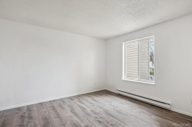 spare room featuring a baseboard heating unit, wood finished floors, a textured ceiling, and baseboards