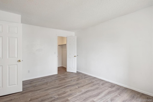 unfurnished bedroom with wood finished floors, a textured ceiling, baseboards, and a closet