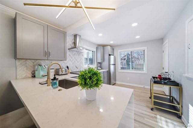 kitchen with wall chimney exhaust hood, gray cabinets, decorative backsplash, light hardwood / wood-style floors, and stainless steel refrigerator