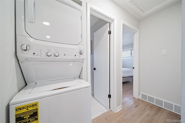 laundry area with light hardwood / wood-style flooring and stacked washer and clothes dryer