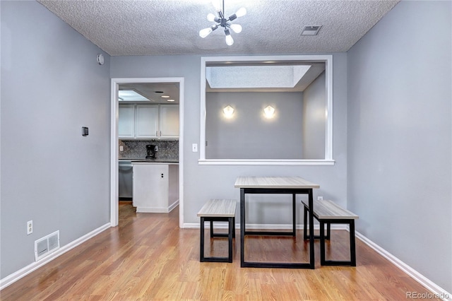 dining area with a textured ceiling, light hardwood / wood-style flooring, and an inviting chandelier