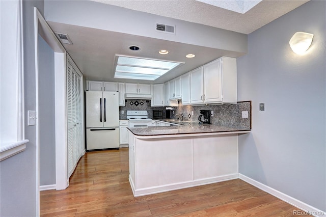 kitchen featuring white appliances, kitchen peninsula, decorative backsplash, sink, and white cabinetry