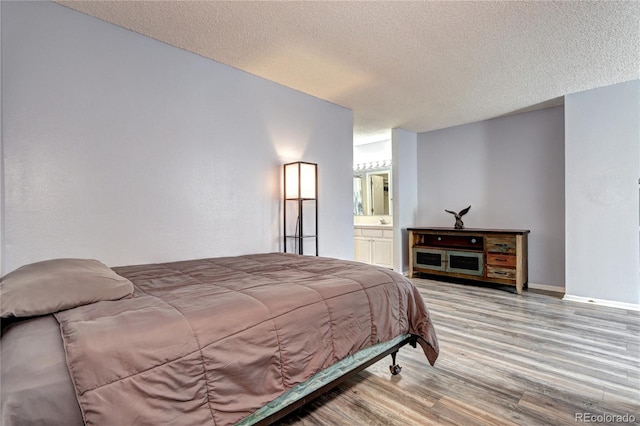 bedroom featuring a textured ceiling, light wood-type flooring, and connected bathroom