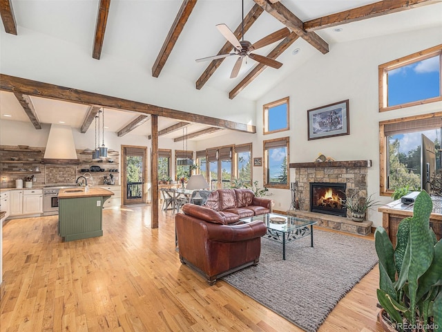 living room with a fireplace, ceiling fan, light wood-type flooring, high vaulted ceiling, and beamed ceiling