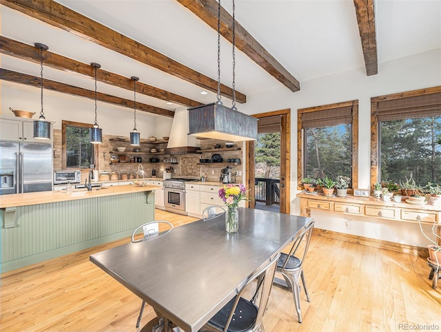 dining room with beam ceiling, a healthy amount of sunlight, sink, and light hardwood / wood-style floors