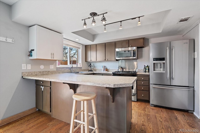 kitchen with a raised ceiling, sink, white cabinets, and appliances with stainless steel finishes