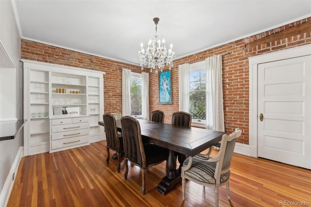 dining room featuring hardwood / wood-style flooring, brick wall, and an inviting chandelier