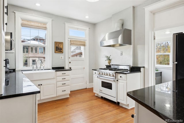 kitchen featuring wall chimney range hood, light hardwood / wood-style flooring, stainless steel fridge, high end stove, and white cabinets