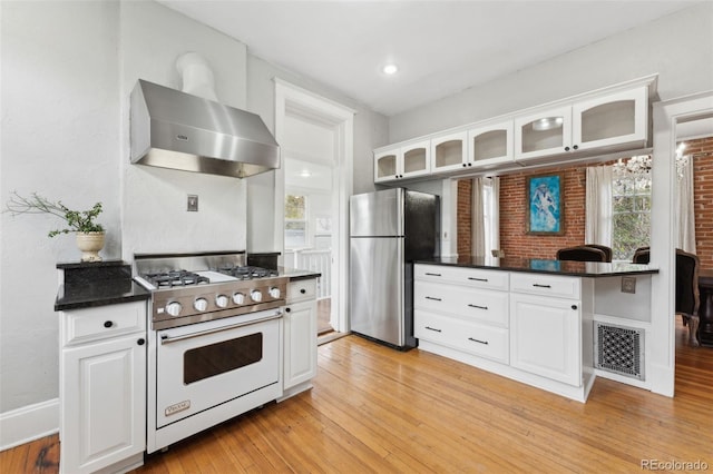 kitchen featuring stainless steel refrigerator, high end stove, white cabinetry, light hardwood / wood-style floors, and wall chimney exhaust hood