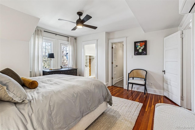 bedroom featuring dark wood-type flooring, ceiling fan, a wall unit AC, a walk in closet, and a closet