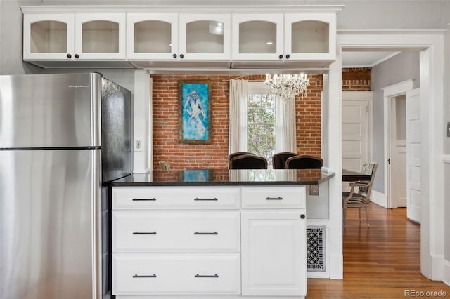 kitchen with wood-type flooring, dark stone countertops, stainless steel refrigerator, brick wall, and white cabinets