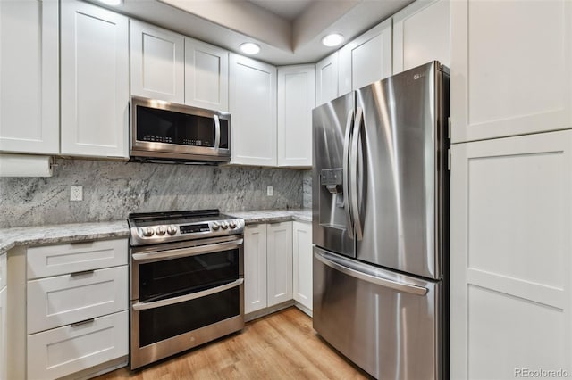 kitchen featuring tasteful backsplash, appliances with stainless steel finishes, light stone countertops, light wood-style floors, and white cabinetry