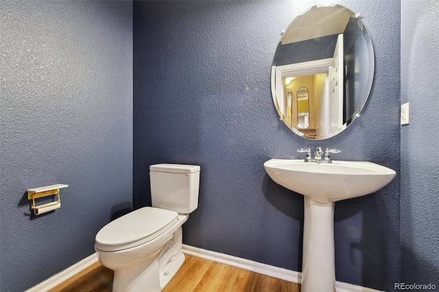 bathroom with toilet, baseboards, wood finished floors, and a textured wall