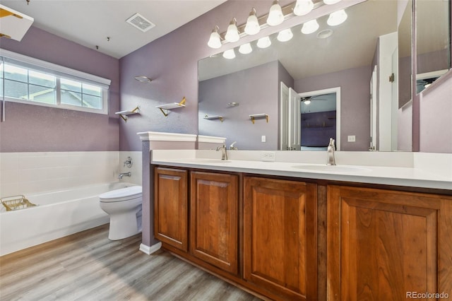 bathroom featuring double vanity, visible vents, wood finished floors, a garden tub, and a sink