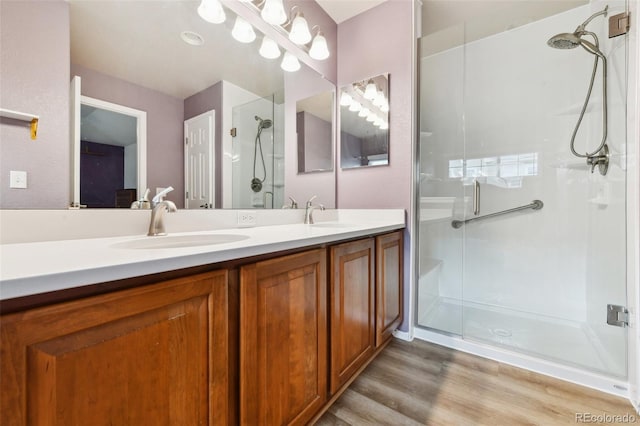 full bathroom with double vanity, a sink, a shower stall, and wood finished floors