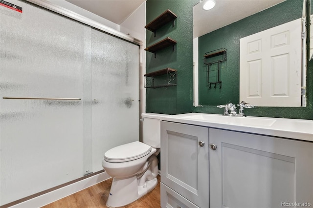 bathroom with a textured wall, toilet, a stall shower, vanity, and wood finished floors