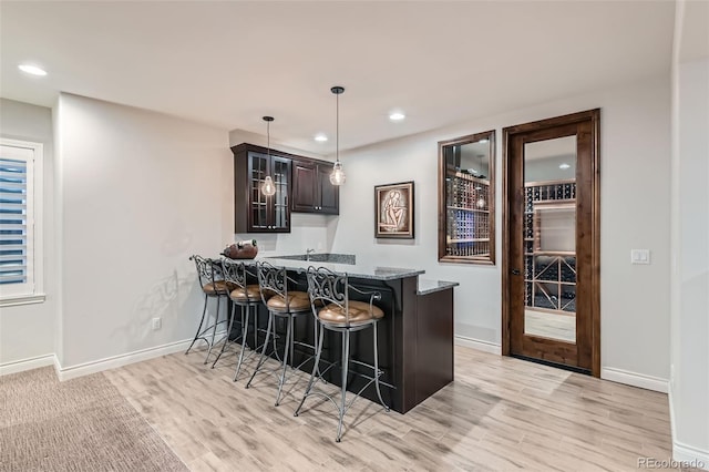 bar featuring stone countertops, hanging light fixtures, dark brown cabinets, and light hardwood / wood-style flooring