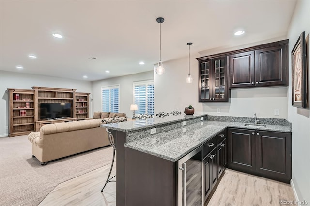 kitchen featuring a breakfast bar, sink, pendant lighting, beverage cooler, and light stone countertops