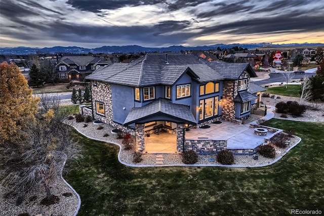 back house at dusk featuring a yard, a mountain view, a fire pit, and a patio area