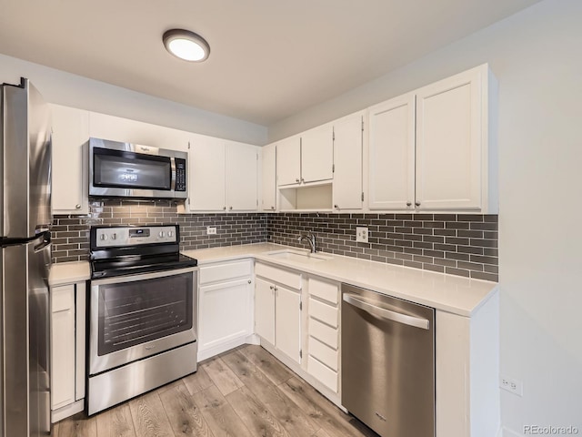 kitchen with sink, light hardwood / wood-style flooring, appliances with stainless steel finishes, white cabinetry, and decorative backsplash