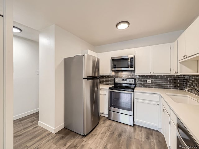 kitchen with appliances with stainless steel finishes, tasteful backsplash, white cabinetry, sink, and light hardwood / wood-style flooring