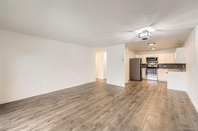 750 S Clinton St Unit 2C, Denver, CO 80247 - unfurnished living room featuring a textured ceiling, light wood-style flooring, baseboards, and a sink