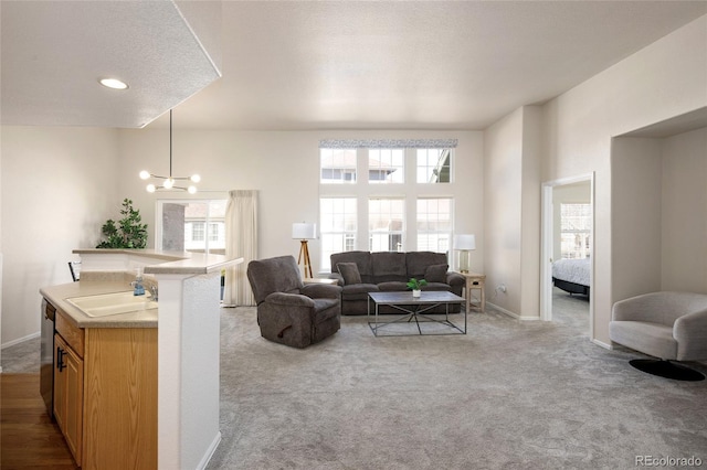 carpeted living area with a notable chandelier, a textured ceiling, a sink, and baseboards