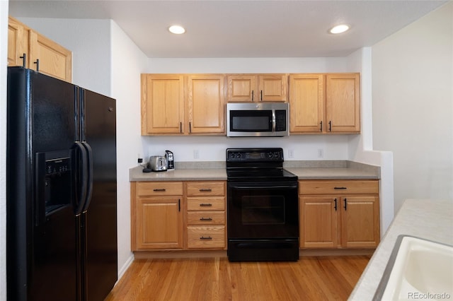 kitchen featuring light wood-type flooring, black appliances, light countertops, and a sink