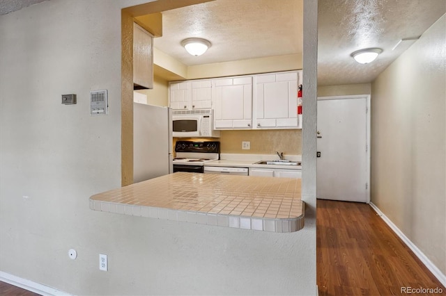 kitchen with tile counters, white appliances, a peninsula, white cabinets, and a sink