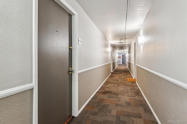 corridor with a textured ceiling, a textured wall, baseboards, and carpet floors