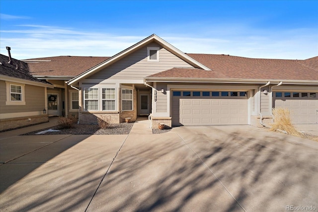 view of front facade featuring a shingled roof, concrete driveway, brick siding, and an attached garage