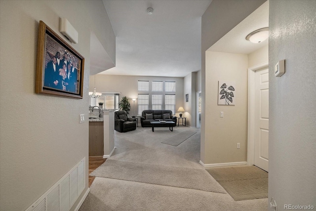 hallway with visible vents, baseboards, light colored carpet, an inviting chandelier, and a sink