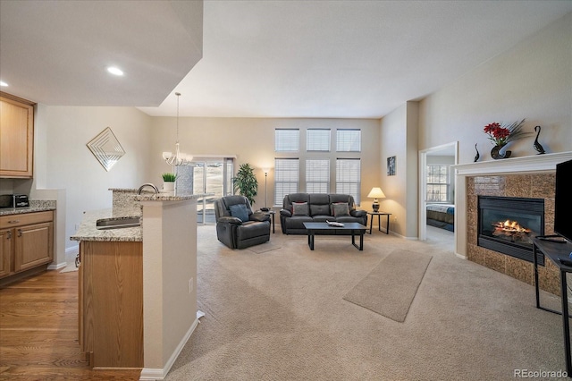 living area featuring a tile fireplace, light colored carpet, a notable chandelier, and baseboards