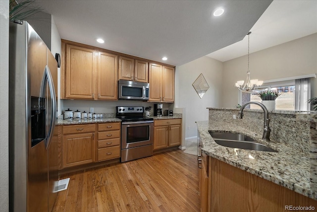 kitchen with light stone counters, light wood-style flooring, a sink, hanging light fixtures, and appliances with stainless steel finishes