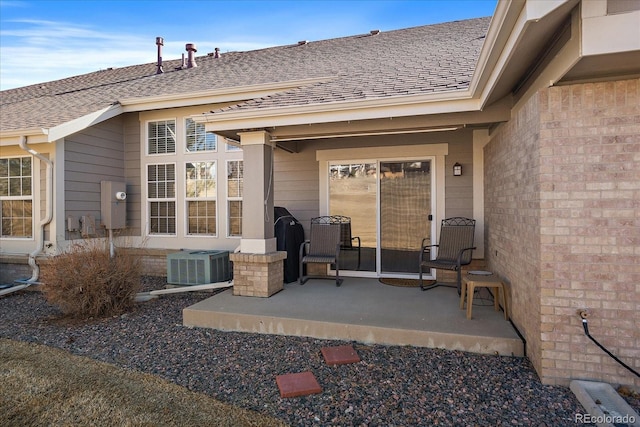 exterior space featuring central air condition unit, brick siding, a shingled roof, and a patio