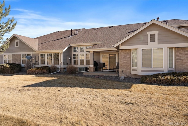 rear view of house featuring brick siding, a patio, roof with shingles, central air condition unit, and a lawn