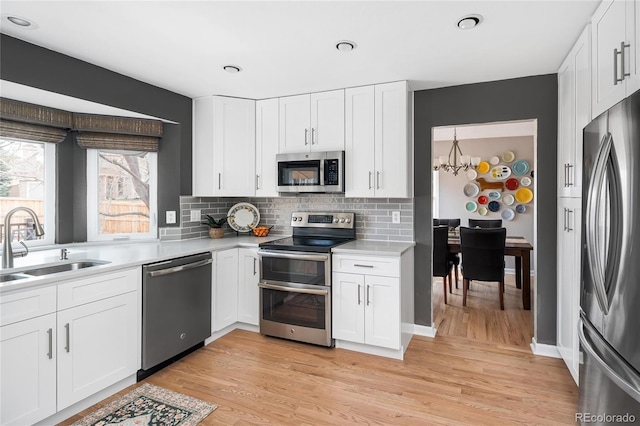 kitchen with a chandelier, light wood-type flooring, light countertops, appliances with stainless steel finishes, and a sink