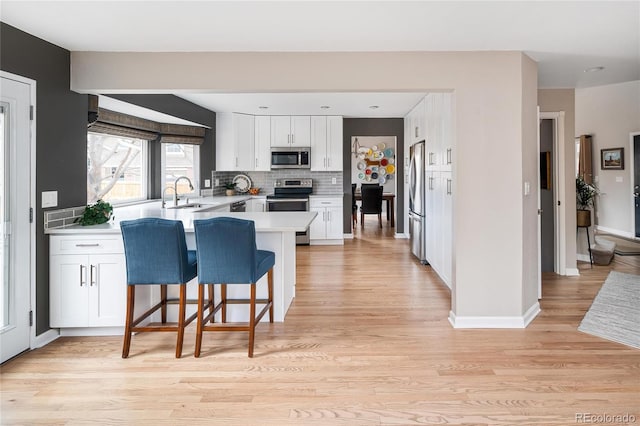 kitchen with white cabinetry, a peninsula, a sink, appliances with stainless steel finishes, and a kitchen bar