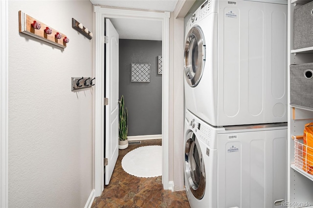 laundry room featuring laundry area, stacked washer and clothes dryer, stone finish flooring, and baseboards