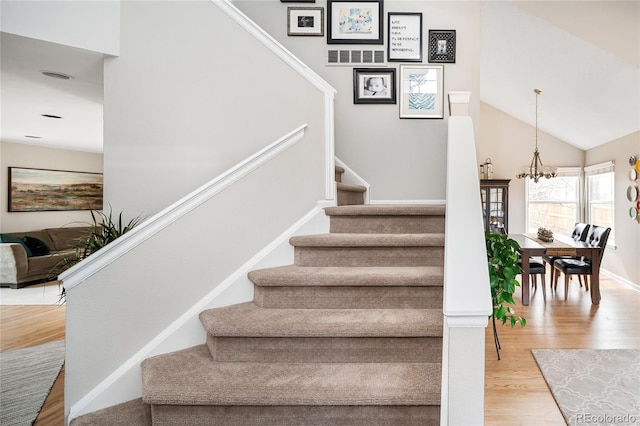 staircase featuring a chandelier, vaulted ceiling, baseboards, and wood finished floors